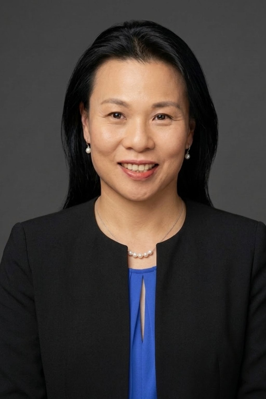 Professional headshot of an Asian woman with long black hair, wearing a black blazer and blue top, smiling against a gray background