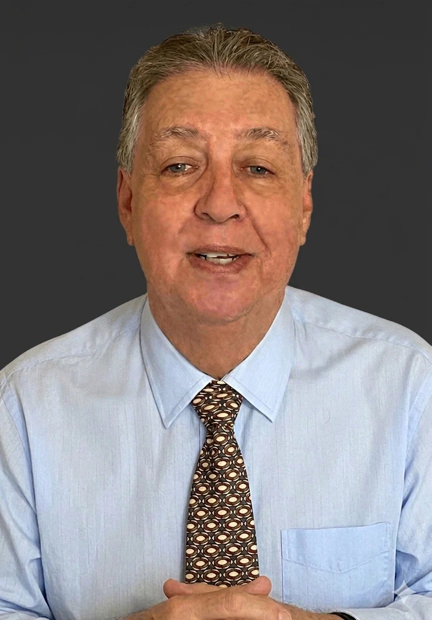 Middle-aged man with gray hair wearing light blue dress shirt and patterned brown tie, smiling at camera against gray background