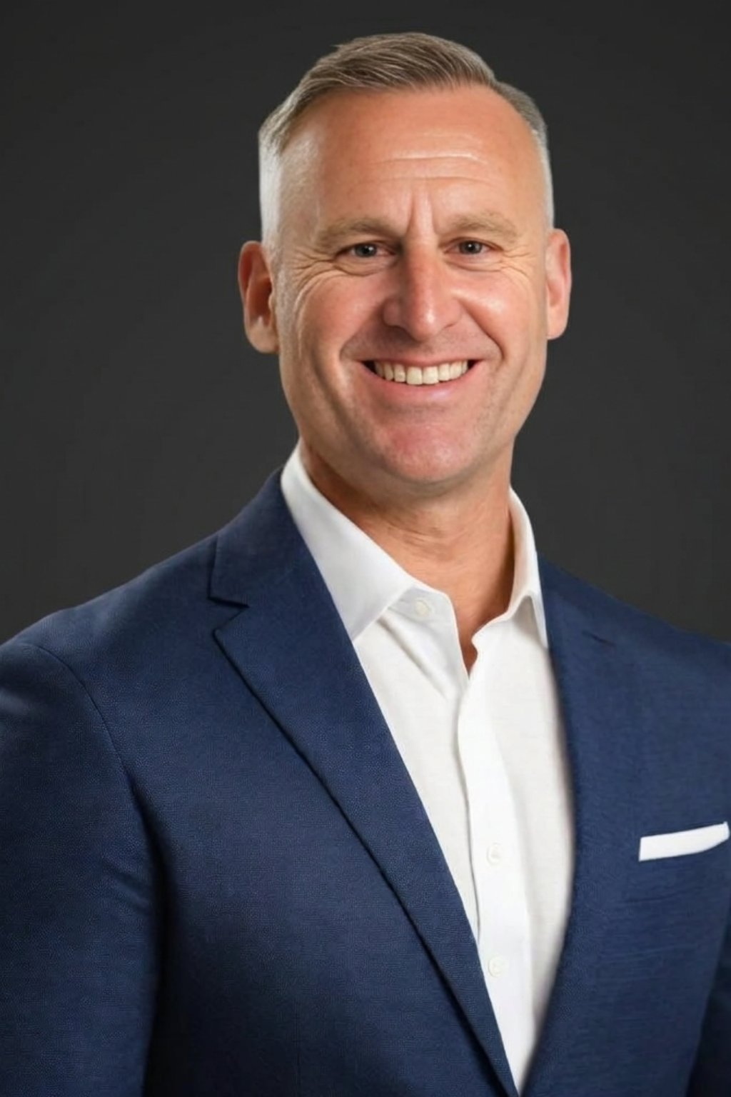 Portrait of a smiling middle-aged man in a dark blue blazer and white dress shirt against a gray background
