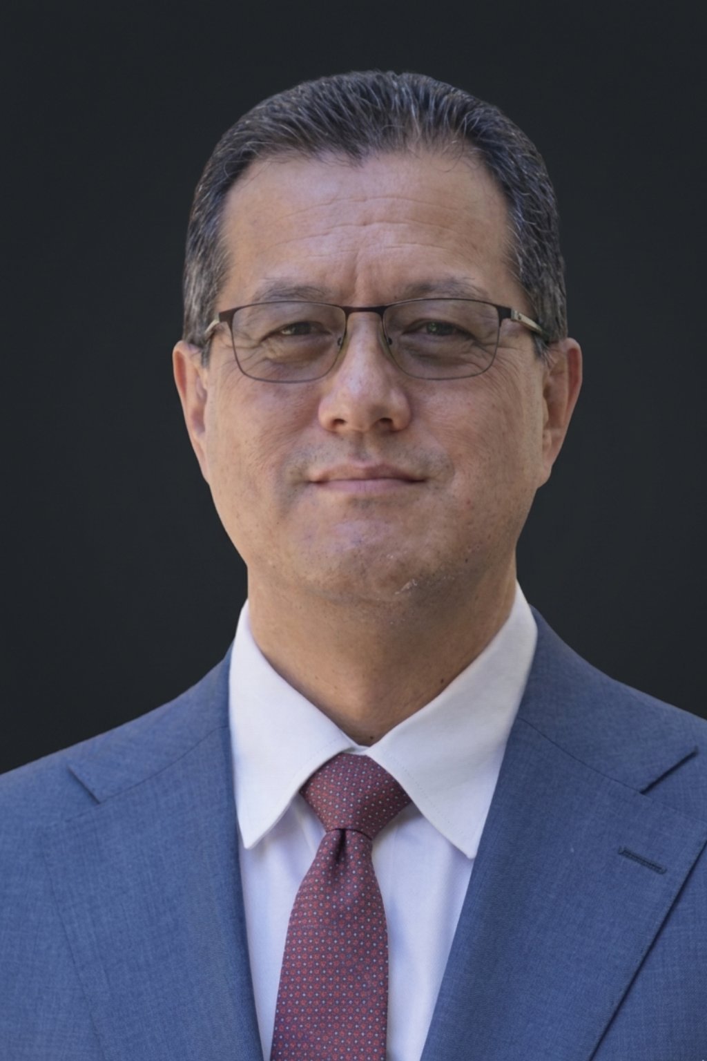 Professional headshot of a middle-aged man wearing glasses, blue blazer, white shirt, and burgundy tie against a dark background
